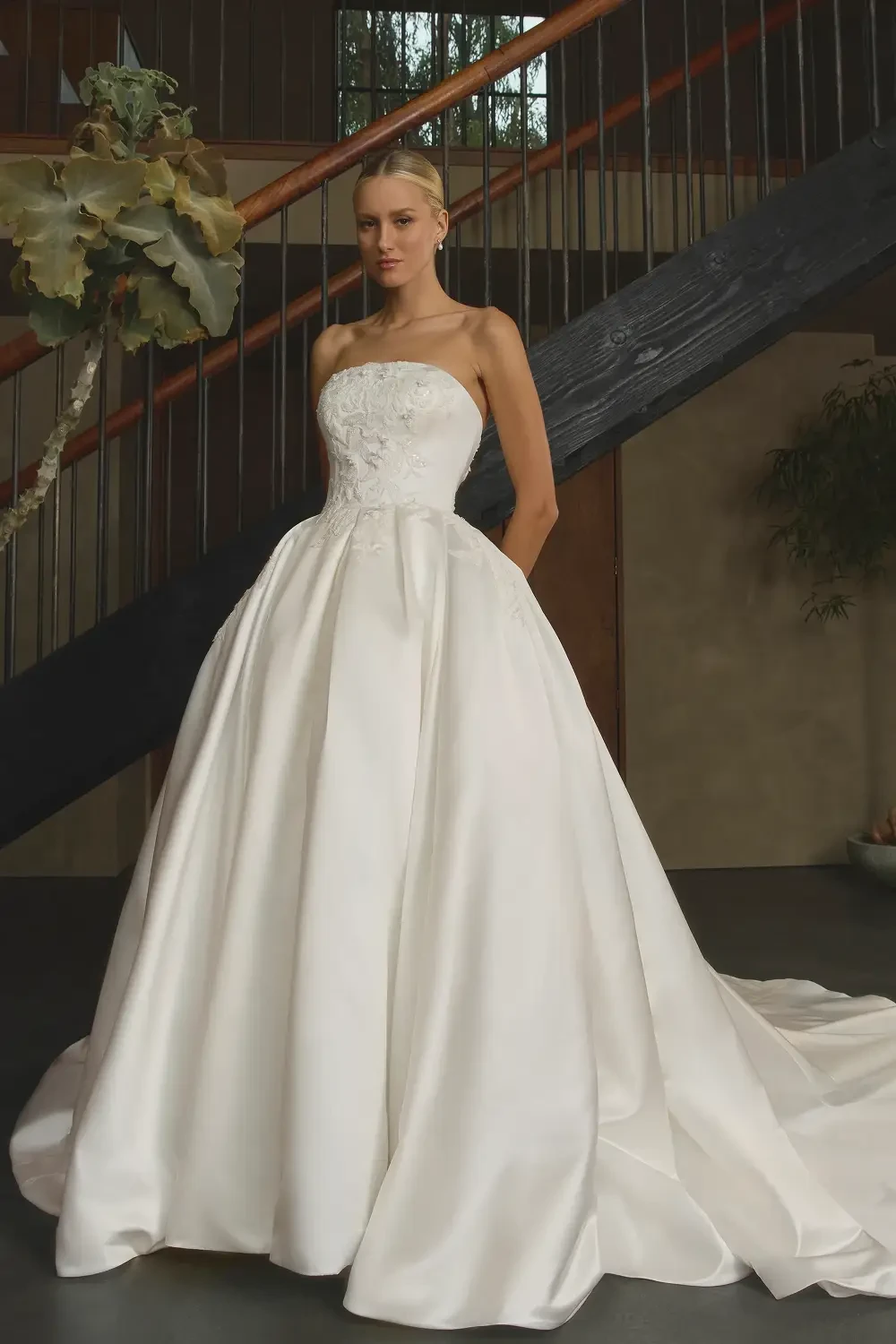A model wearing a strapless white wedding gown standing on a staircase.