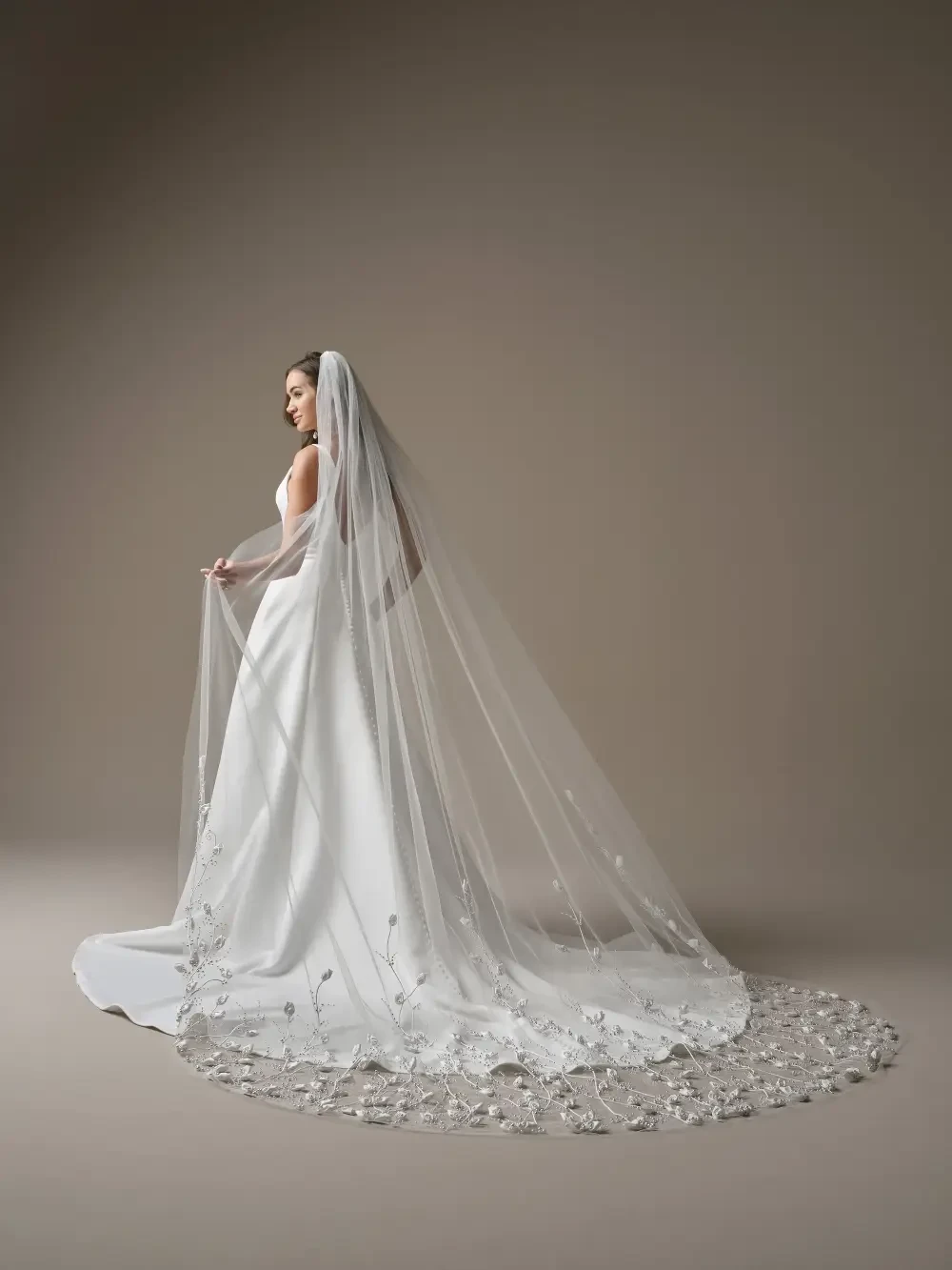A woman wearing a simple, elegant white wedding dress with a fitted bodice and flowing skirt, standing against a neutral background.
