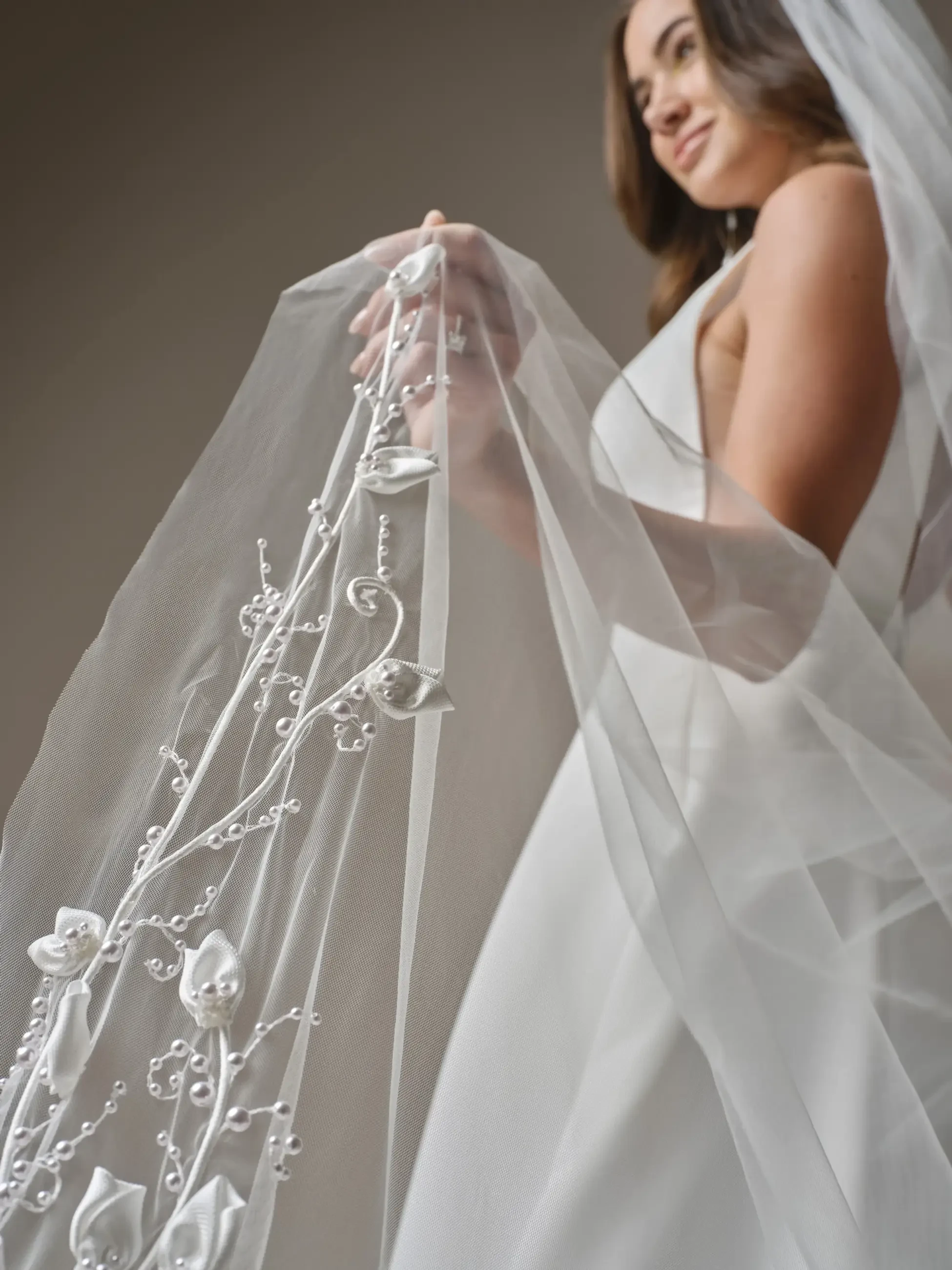 A bride holds up a sheer, embroidered veil with floral decorations.