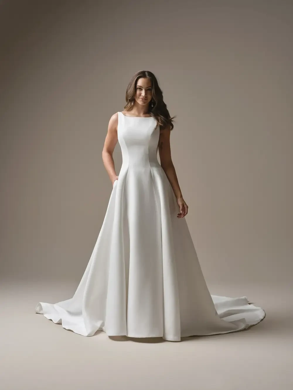 A woman in a sleek, white wedding dress with a fitted bodice and flowing skirt, standing against a neutral background.