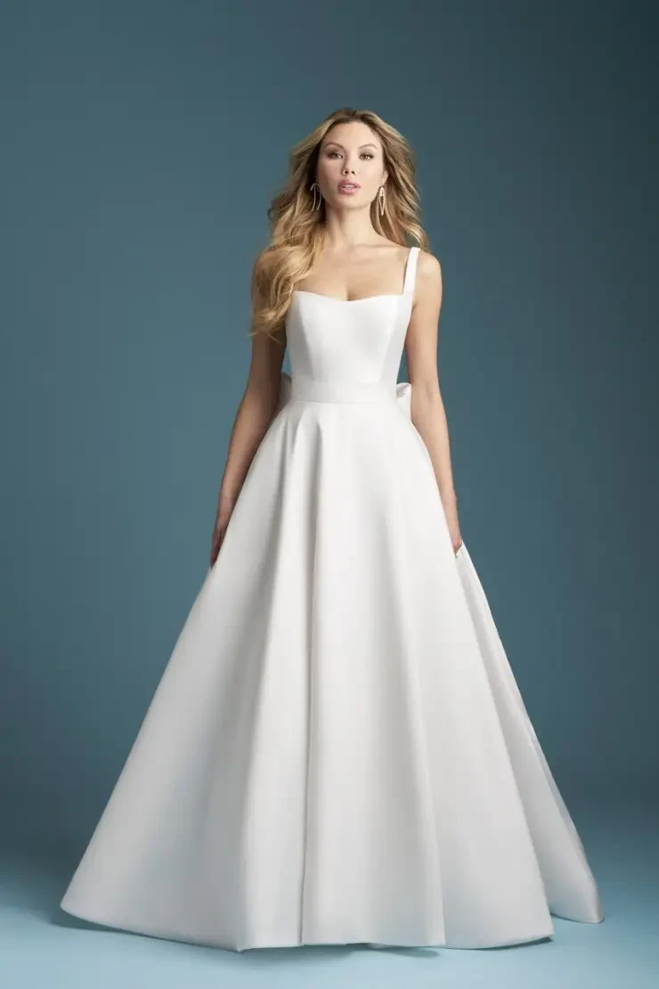 A woman in a long, elegant white gown with a fitted bodice and a full skirt, standing against a blue background.