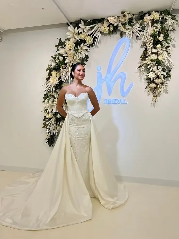 model is wearing a strapless sheath bridal gown with an overskirt