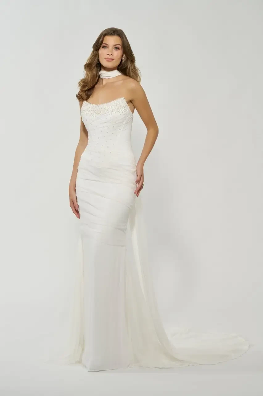 A woman in a elegant white wedding gown with intricate detailing, posing against a neutral background.