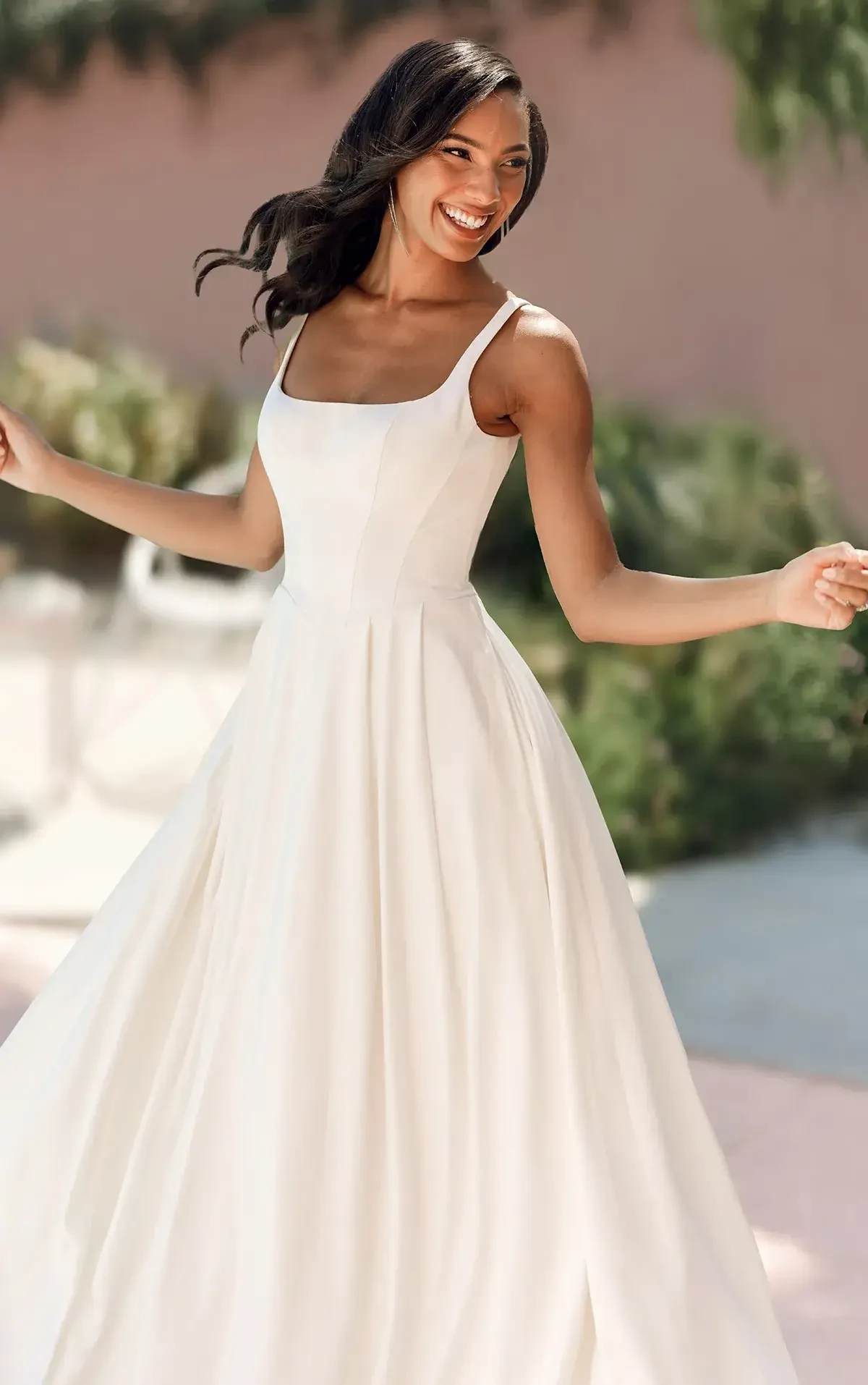 A woman is joyfully twirling in a flowing white dress with a square neckline.