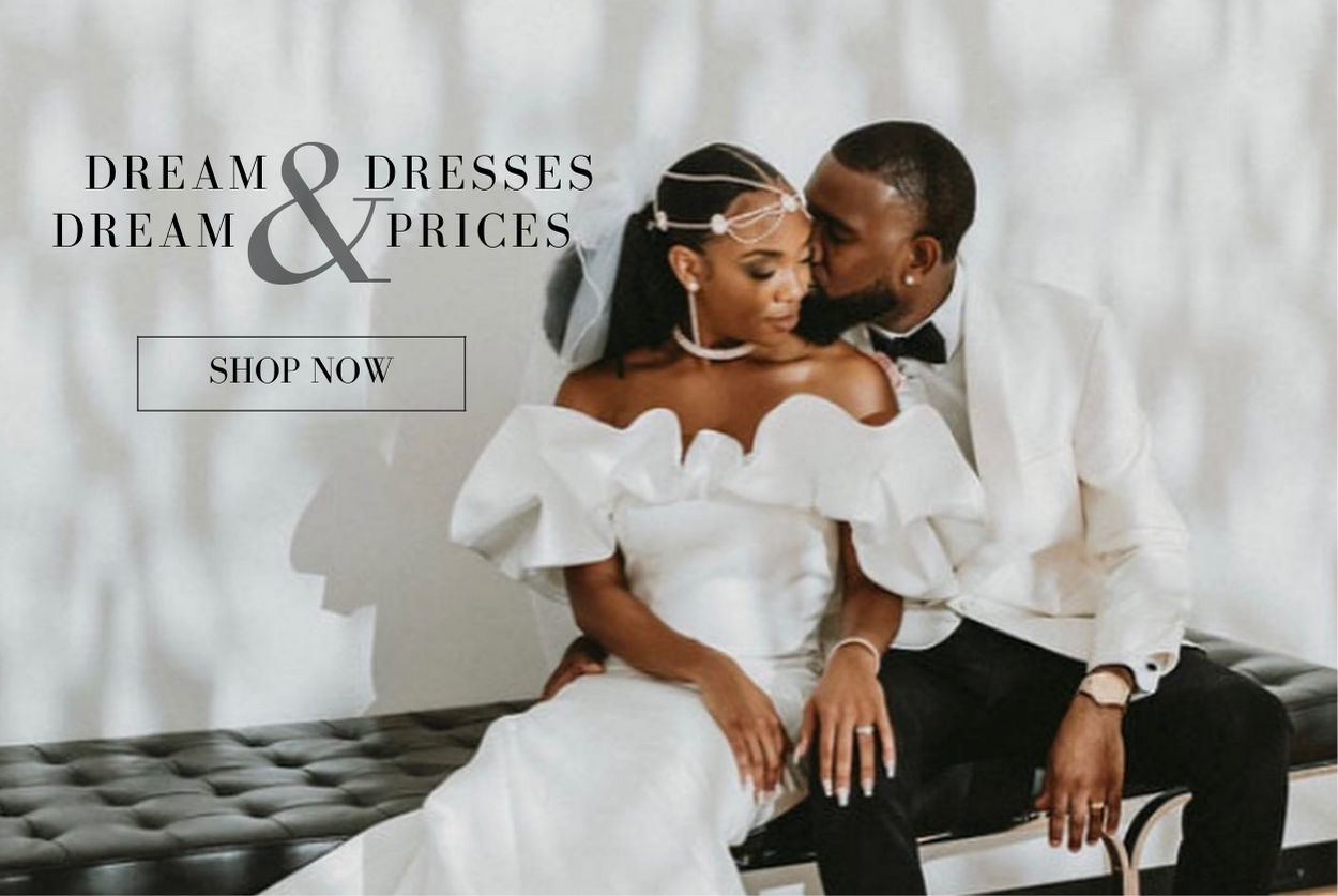 DREAM DRESSES AND DREAM PRICES SHOP NOW NEWLY WEDS SITTING LOVINGLY ON BENCH WHILE BRIDE WEARS MODERN OFF THE SHOULDER WEDDING GOWN WITH A STRUCTURAL PUFF NECKLINE AND GROOM WEARS WHITE TUXEDO BLAZER AND BLACK DRESS PANTS
