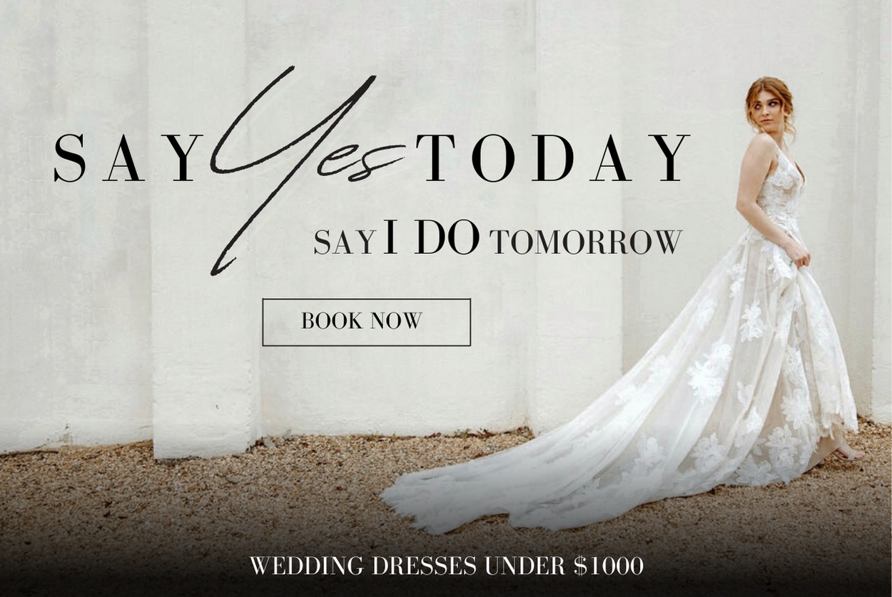 SAY YES TODAY SAY I DO TOMORROW. OFF THE RACK WEDDING DRESSES UNDER $1000. BRIDE IS WEARING A-LINE WEDDING GOWN AND WALKING ALONG A WHITE CEMENT WALL ON A GRAVEL PATH WHILE LOOKING OVER HER SHOULDER AND PICKING UP HER DRESS AS SHE WALKS