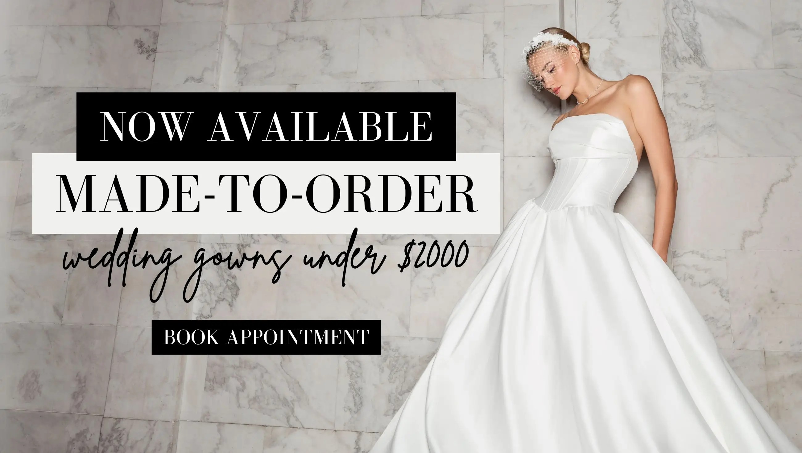 ONE OF A KIND WEDDING DRESSES SHOP IN STORE. BRIDE WEARS LONG SLEEVES LACE WEDDING DRESS WITH SHEER BODICE AND IS SEATED IN A VINTAGE CHAIR WITH WHITE CURTAINS BEHIND HER, LEANING ON HER HAND WHILE HER OTHER ARM IS OUTSTRETCHED ALONG HER CROSSED LEGS.